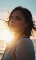 a woman looks off into the distance and stands against a beach sunset