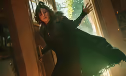 a woman in a black outfit and coat standing near an open window