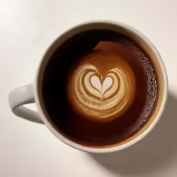 a heart coffee is on top of a white saucer