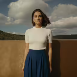 a woman leaning against a wall wearing a white top
