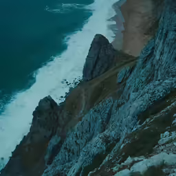 a bird flying over a rocky outcropping next to the beach