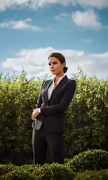 a woman in a business suit leaning on a bush