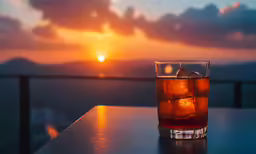 a glass of alcohol sits on a ledge with the sun setting