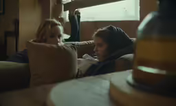 a woman sitting on a couch next to a woman who is reading