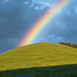 a rainbow is lit up above a grassy hillside