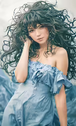 a woman is standing in a blue dress with her hair blowing in the wind