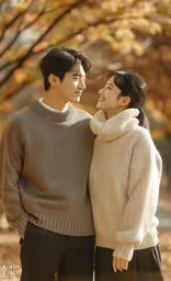 a man and a woman standing together in front of trees,a woman holding the arms of a man in front of some trees