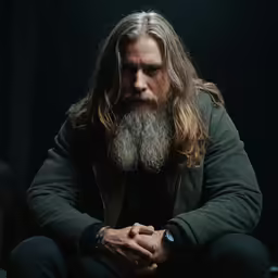 man with long hair and a beard sitting in a chair