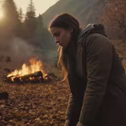 a girl in the woods looking at a burning log