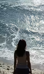 a girl sits on the beach near the water