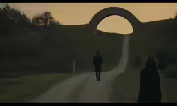 a man and a woman walking down the road near a large arch