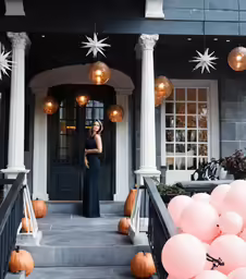 a woman stands in front of a house with pumpkins on the ground