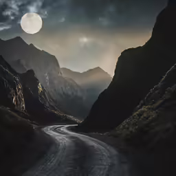a mountain road with an almost full moon and some mountains