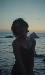 a girl is standing on the beach at sunset