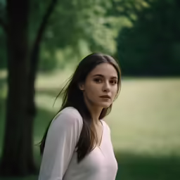 a woman standing in the grass near a tree