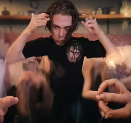 the young man is touching his forehead as other hands hold him up and show off his piercing