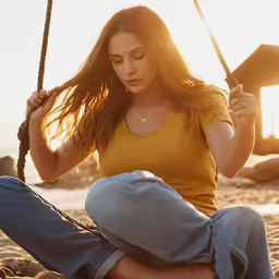a woman sitting on the sand holding a wooden swing