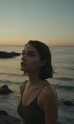 a woman with dark hair standing on the beach during the sunset