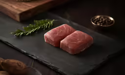 a pair of raw steaks on slate sit next to some nuts