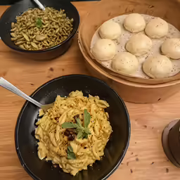 three black plates with noodles and vegetables on wooden table