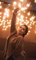 the woman in brown is standing under a large bunch of lights