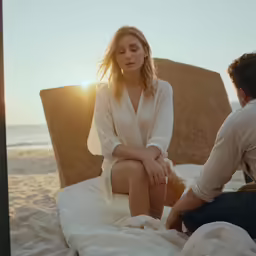 man and woman sit on white towels at the beach in the sunset