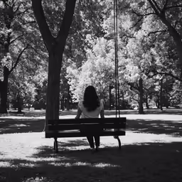 a woman sitting on a bench next to a tree