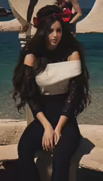 a beautiful woman sitting on a post with water and sand
