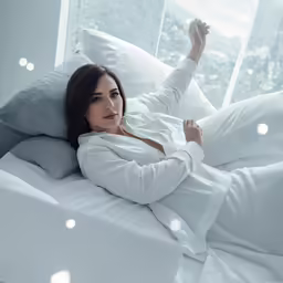 a woman laying in bed with her hands up in the air