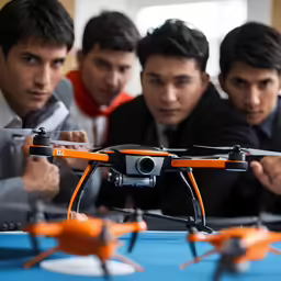 three men looking at a small orange and black propeller controlled unmanned