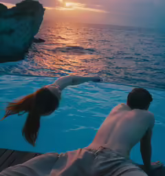 the couple is floating in a swimming pool looking at the ocean