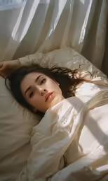 a woman lying in bed with white sheets