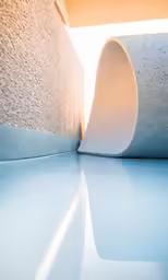 the corner of a concrete building with a blue surface and sunlight streaming down on it