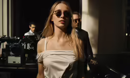 a woman wearing shades is standing next to a camera man