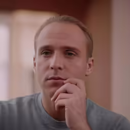 man in grey shirt looking off into distance with one hand on his chin