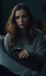 a woman sits on a couch and looks at her phone