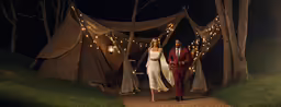 two people dressed in wedding attire stand under fairy lights
