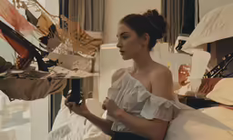 a woman sitting on a bed holding a bottle in her right hand