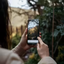 a woman holding up a smartphone with an image of a forest on it