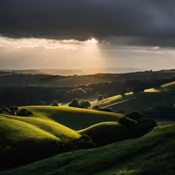 the sun peeks through dark clouds over the rolling hills