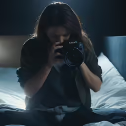 a woman sitting on a bed while holding a camera