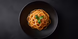 a dish with noodles and basil on a black plate