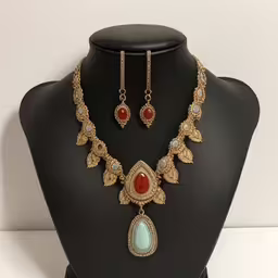 this necklace set is on a mannequin for display,a necklace and earring set with two beads on a mannequin head,an image of a necklace and matching earrings on display,the necklace is adorned with a beautiful pendant and earring,an image of a necklace set with stone and gems
