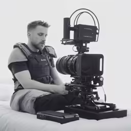 the man is sitting next to a camera on the bed