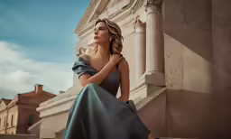 a woman in a blue gown leaning against a building