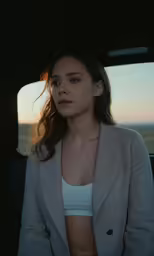 a woman standing in the back of a car, her jacket pulled back and wearing a bra