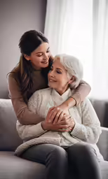 mother hugging daughter on the cheek while she is sitting on the couch