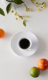 a cup of coffee sitting next to three fruits