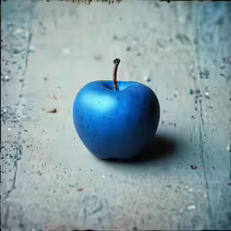 a blue apple laying on the ground, on some concrete