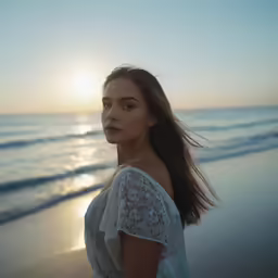 a woman stands on the beach at sunset